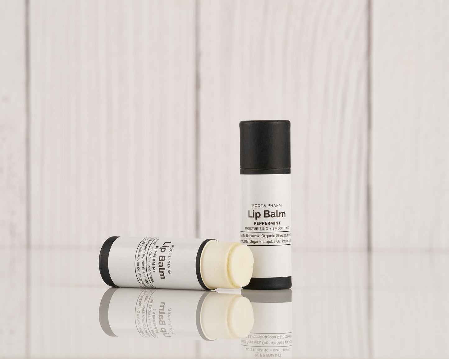 Peppermint Lip Balm in a white twist-up tube with black cap, partially opened and lying next to its lid on a reflective surface.