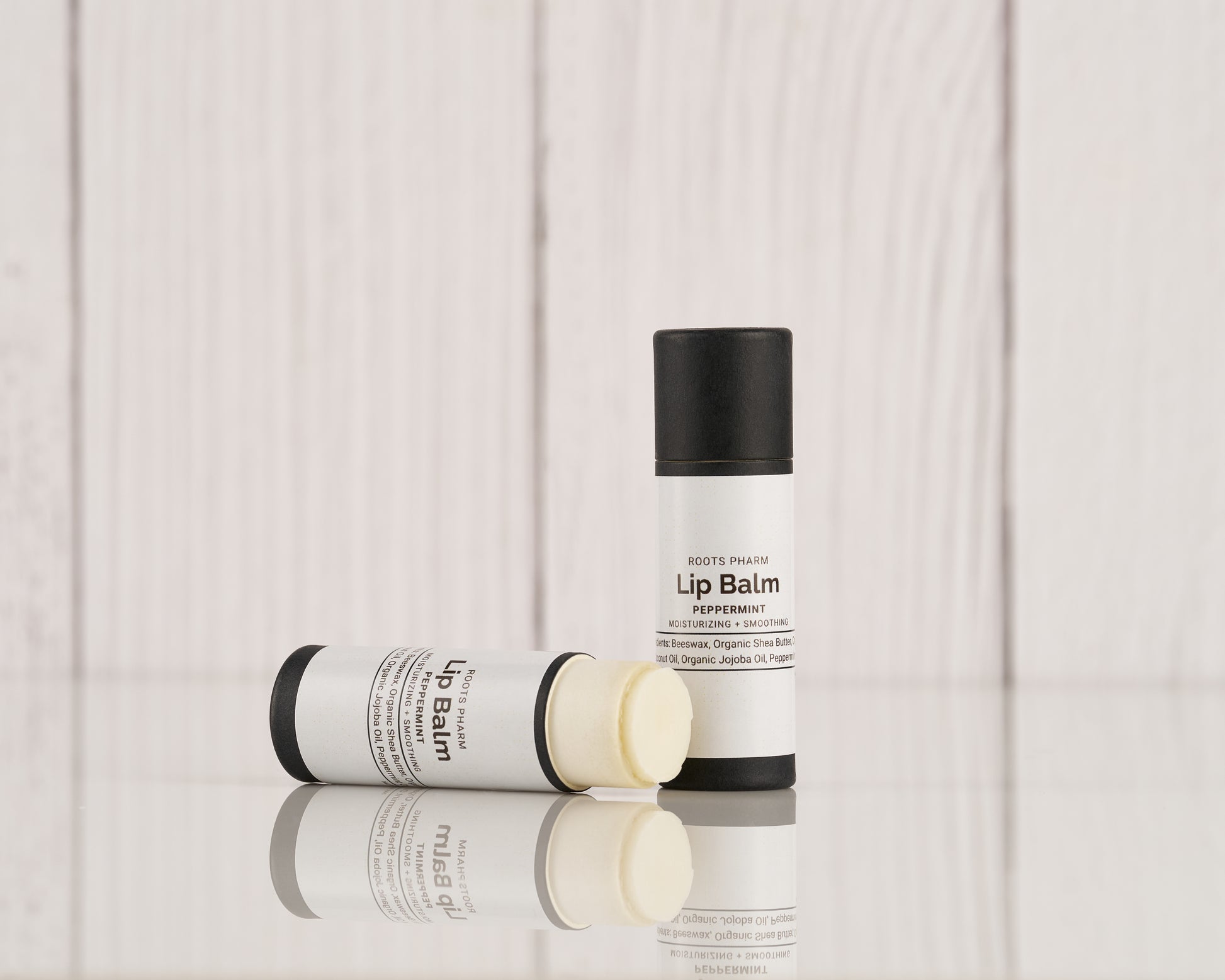 Peppermint Lip Balm in a white twist-up tube with black cap, partially opened and lying next to its lid on a reflective surface.